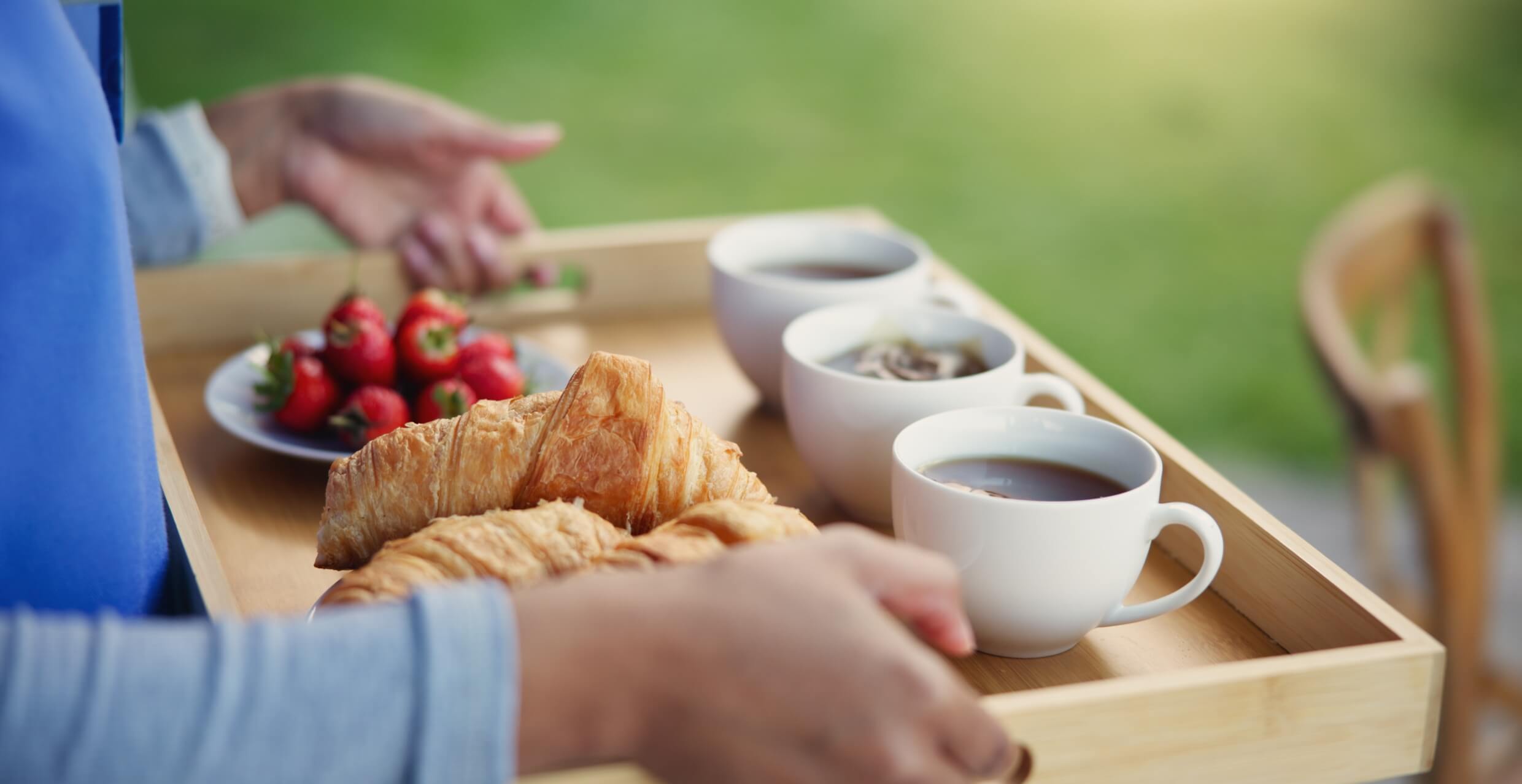 Close up of woman carrying breakfast tray with croissants, tea, coffee, strawberries