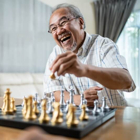 Older Asian American male smiling, playing chess