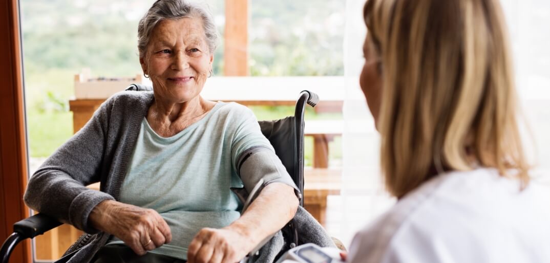 Female caregiver in foreground, older woman smiling in wheelchair