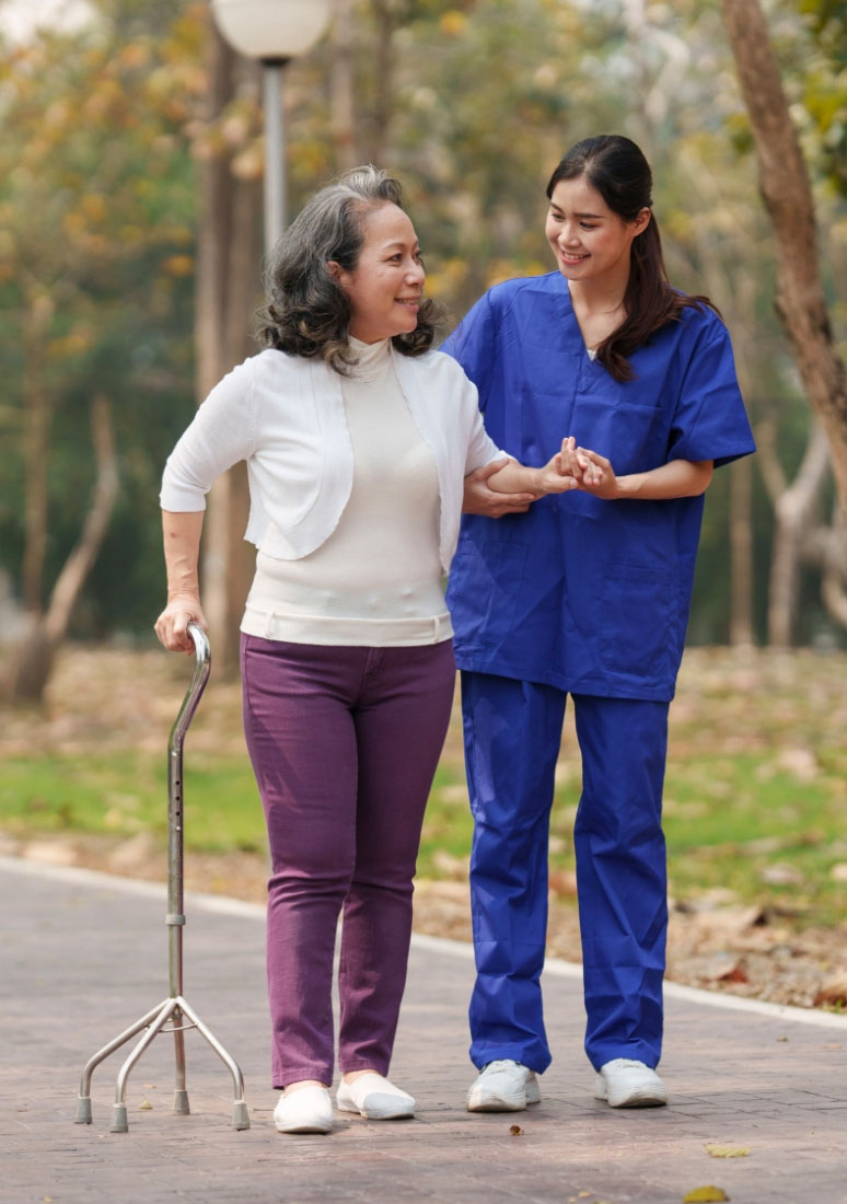 Female caregiver supporting older woman walking with cane