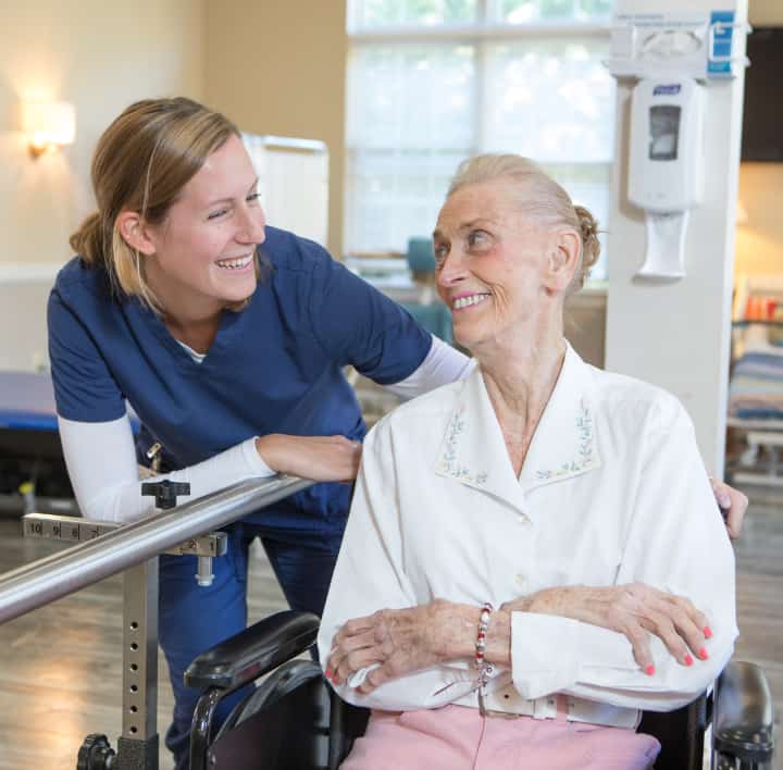 Female caregiver supporting older female in wheelchair