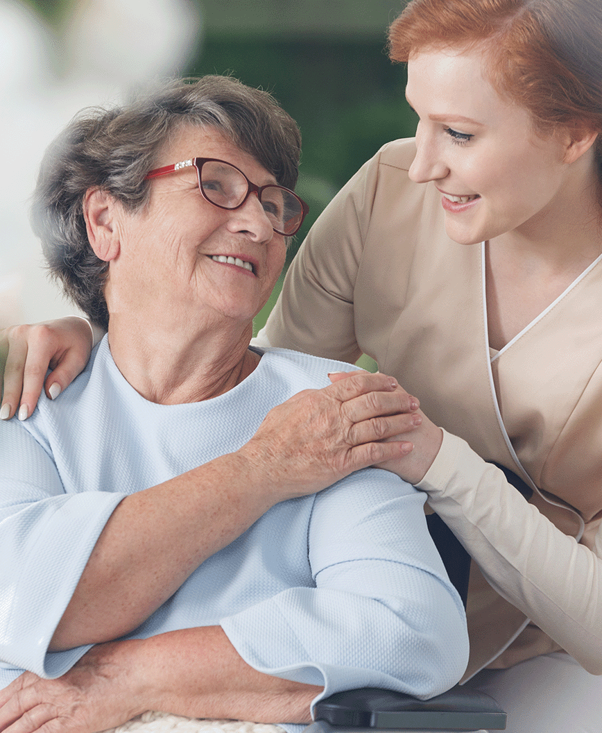 Female caregiver holding hand of older female, both smiling, supportive care